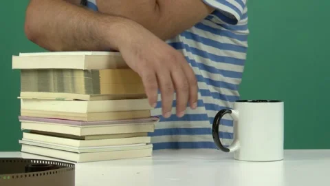 Man Leaning on Stack of Books with White Cup on Table Green Screen Background Vídeos de archivo 344677376