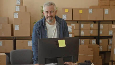 Man leans on desk with computer and stacked parcels, hands on table in buil.. Stockbeeldmateriaal 337437117