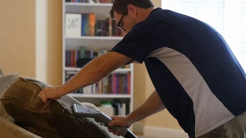 Man leans over as he cleans couch cushion with steam cleaner in slow motion Stock Footage 85864855