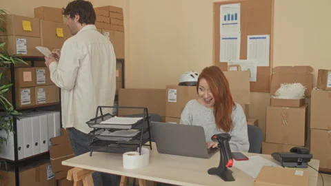 Man leans over laptop while woman smiles and clasps hands amid packed boxes.. Stock Footage 337391836