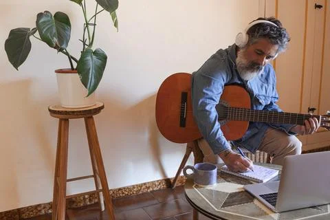 Man learning guitar online using laptop and headphones Foto stock