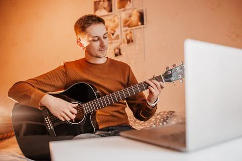 Man learning to play guitar with the help of online learning at home. Guy sit Stock Photos