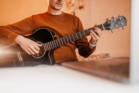 Man learning to play guitar with the help of online learning at home. Guy sit Stock Photos