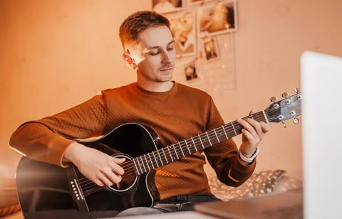 Man learning to play guitar with the help of online learning at home. Guy sit Stock Photos