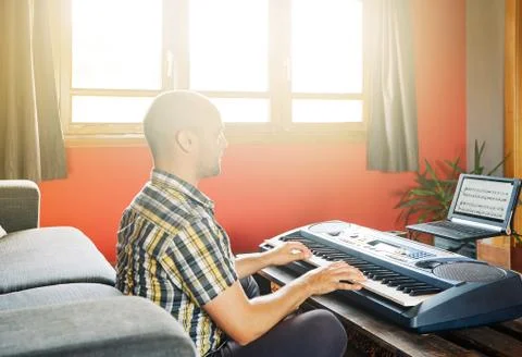 A man learning to play the piano while watching an online course at home Stock Photos