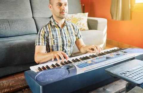 A man learning to play the piano while watching an online course Stock Photos