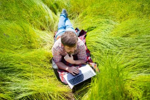 Man learns, working on laptop lying on meadow. mobile Internet in rural. Stock Photos