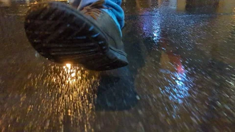 A man in leather boots cross the road on wet asphalt during the rain at night Stock Footage 252228531