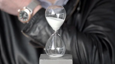 Man with leather jacket and watch looking at hourglass Stockbeeldmateriaal 88647382