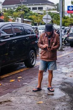 Man in Leather Jacket Checking Phone on a Wet Sidewalk Photos