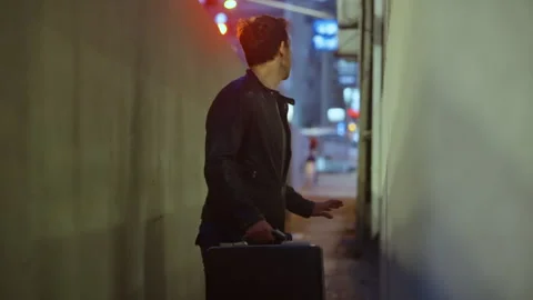 Man in leather jacket clutches a briefcase while cautiously looking back in a 库存影片 313199031