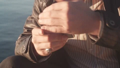 A man in a leather jacket lights a cigarette with a gasoline lighter against the Stock Footage 220667883