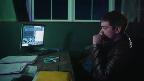 A man in a leather jacket sits and smokes in front of a monitor in the office Stock Footage 249669202