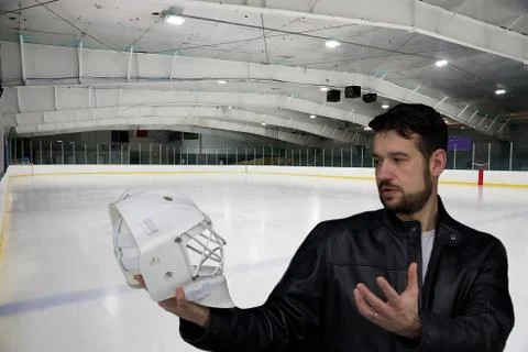 A man in a leather jacket is standing on a ice hockey rink and holding helmet Stock Photos