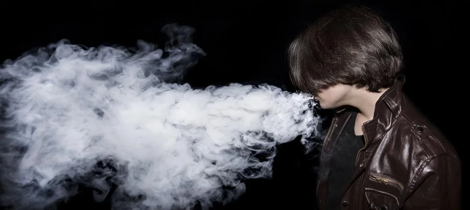 Man a leather jacket  vaping e-cigarette and blowing a cloud on black backgro Stockfoto's
