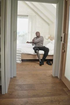Man with leg prosthesis sitting on bed Stock Photos