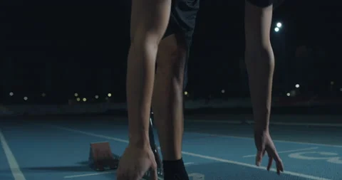 Man with legs prosthesis prepares for launching off the start line at night Stock Footage 154009128