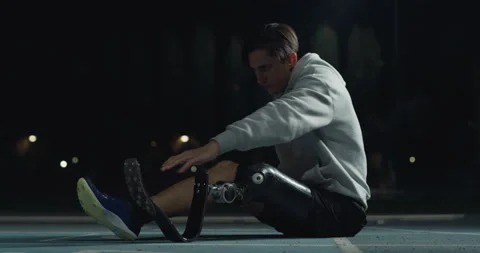 Man with legs prosthesis warms up before run with dedication at night. Stock Footage 154009398
