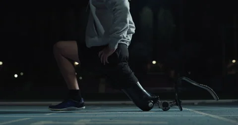 Man with legs prosthesis warms up before run with dedication at night. Stock Footage 154009426