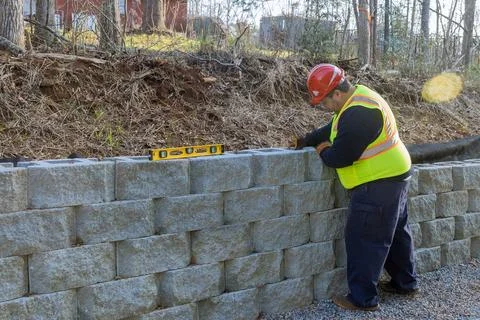 Man with leveling tool building retaining block wall with being built on new Foto stock