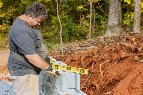 A man levels a tool during the construction of a concrete block retaining wall Foto stock