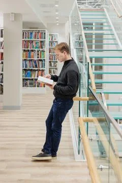 Man in library is reading book sitting on steps of glass staircase Stock Photos