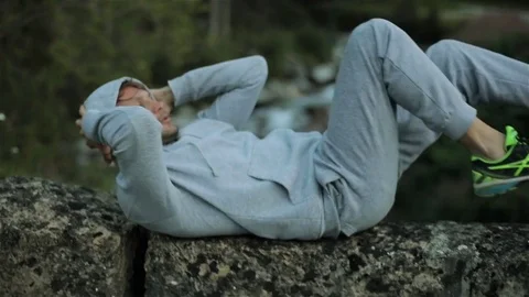 Man lies on back does cross crunches exercising outdoors close up slow motion Stock Footage 79974672