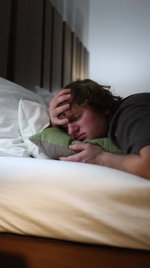 Man lies in bed with hand on head suffering from headache and stress looking exh Stock Footage 318217613