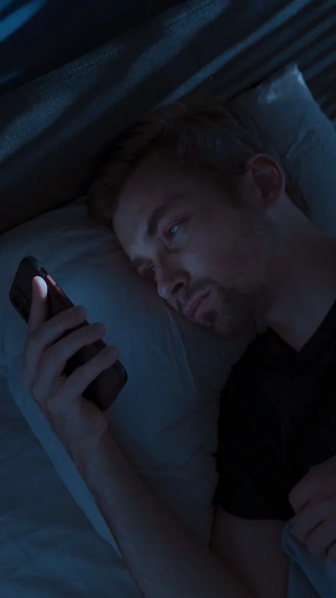 Man lies in bed at night, staring at his smartphone screen, doom scrolling Stock-Footage 315992692