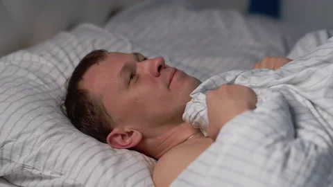 A man lies in a comfortable bed and smiles, dreams before bedtime Stock Footage 130469804