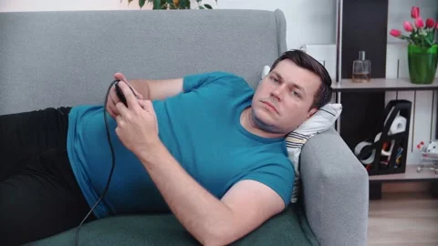 A man lies on the couch in front of the TV in his hands holding a joystick. Stock Footage 147670641