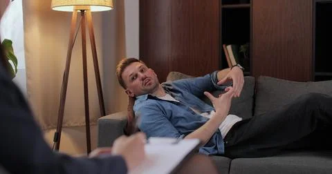Man lies on couch sharing personal life problems in therapy room. Woman 写真素材