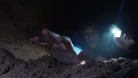 Man lies on ground in cave deeply breathing with effort stretches out his hand Stock Footage 80053546
