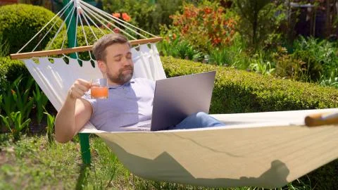 Man lies in hammock, work on computer drink juice. Foto stock