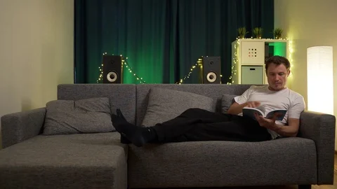 A man lies on the sofa and leafing through a book Stock Footage 129388161