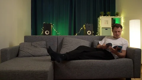 A man lies on the sofa and leafing through a book Stock Footage 129388168