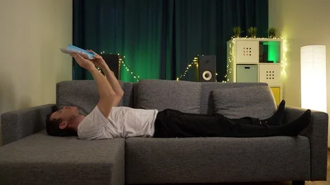 A man lies on the sofa and leafing through a book Stock Footage 129388171