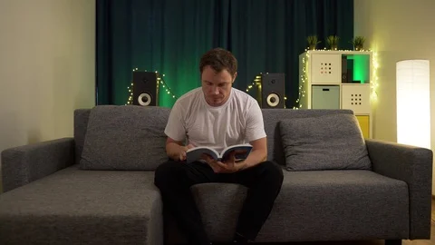 A man lies on the sofa and leafing through a book Stock Footage 129388175