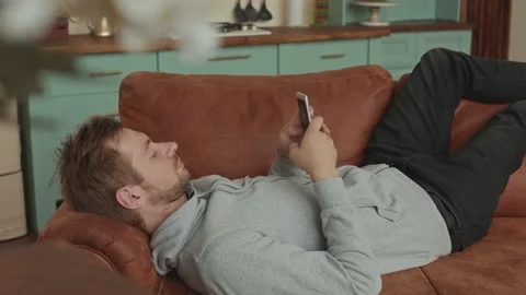 A man lies on a sofa and uses a smartphone. Cozy Living Room Stock Footage 138552477