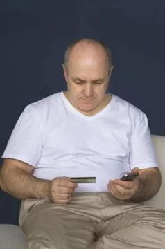 A man lies on a sofa, makes a payment through a smartphone. Stock Photos