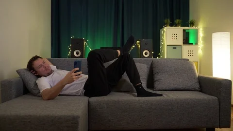 A man lies on the sofa, with the phone Stock Footage 129384358