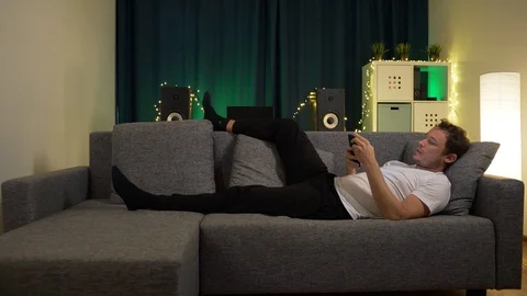 A man lies on the sofa, with the phone Stock Footage 129384486