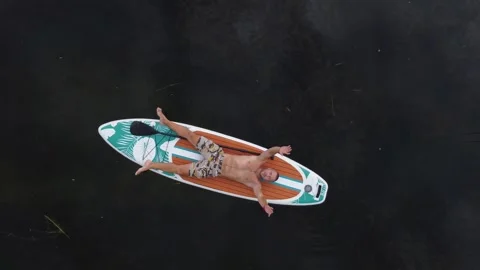 A man lies on a sup board on the surface of the lake. Cinematic top view. Stock-Footage 245262610