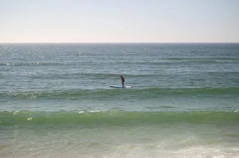 Man with life jacket doing stand up paddleboarding in the sea near the coast Stock Photos