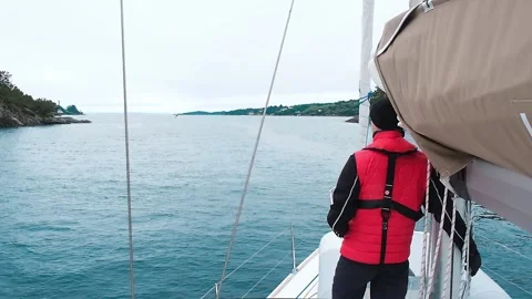 Man in life jacket stands on bow of yacht sailing on sea bay Stock Footage 168364012
