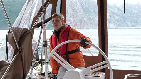 Man with life jacket turns steering wheel in yacht cockpit Stock Footage 168372487