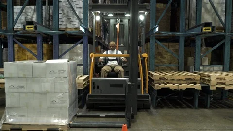 Man lifting and placing pallet on shelving by forklift in warehouse. 動画素材 88104864