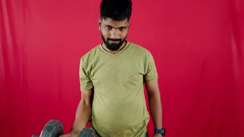 Man lifting dumbbell with effort doing exercise red background Stock Footage 262362240