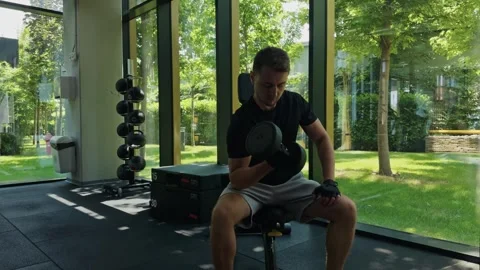 Man lifting dumbbell, engaging in strength training workout inside a fitness cen Stock Footage 339597604
