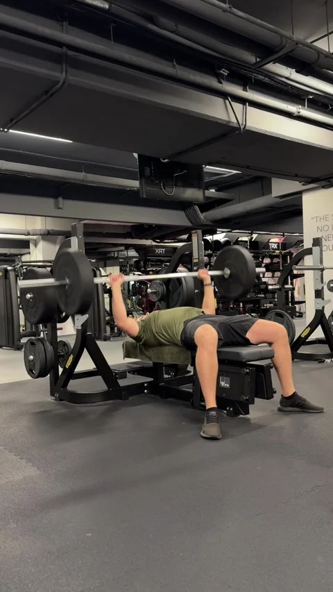 Man lifting heavy barbell while training chest muscles on a bench in a gym Видео 339600712